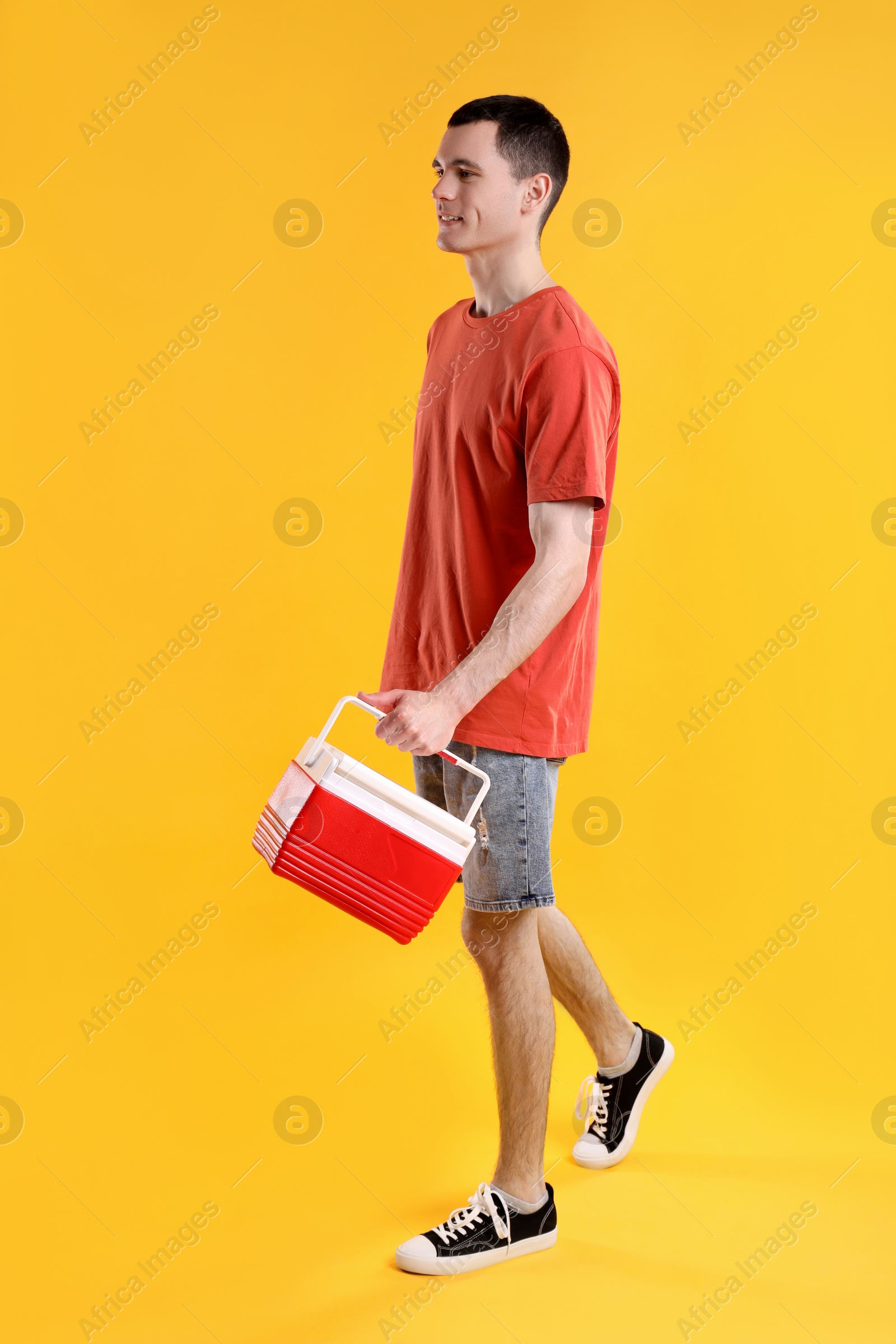 Photo of Man with red cool box walking on orange background