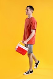 Man with red cool box walking on orange background