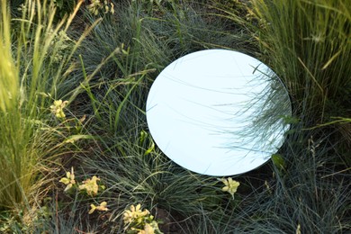 Photo of Round mirror among grass and flowers reflecting sky. Space for text