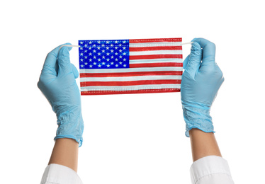 Doctor holding medical mask with USA flag pattern on white background, closeup. Dangerous virus