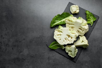 Photo of Cut fresh raw cauliflowers on black table, top view. Space for text