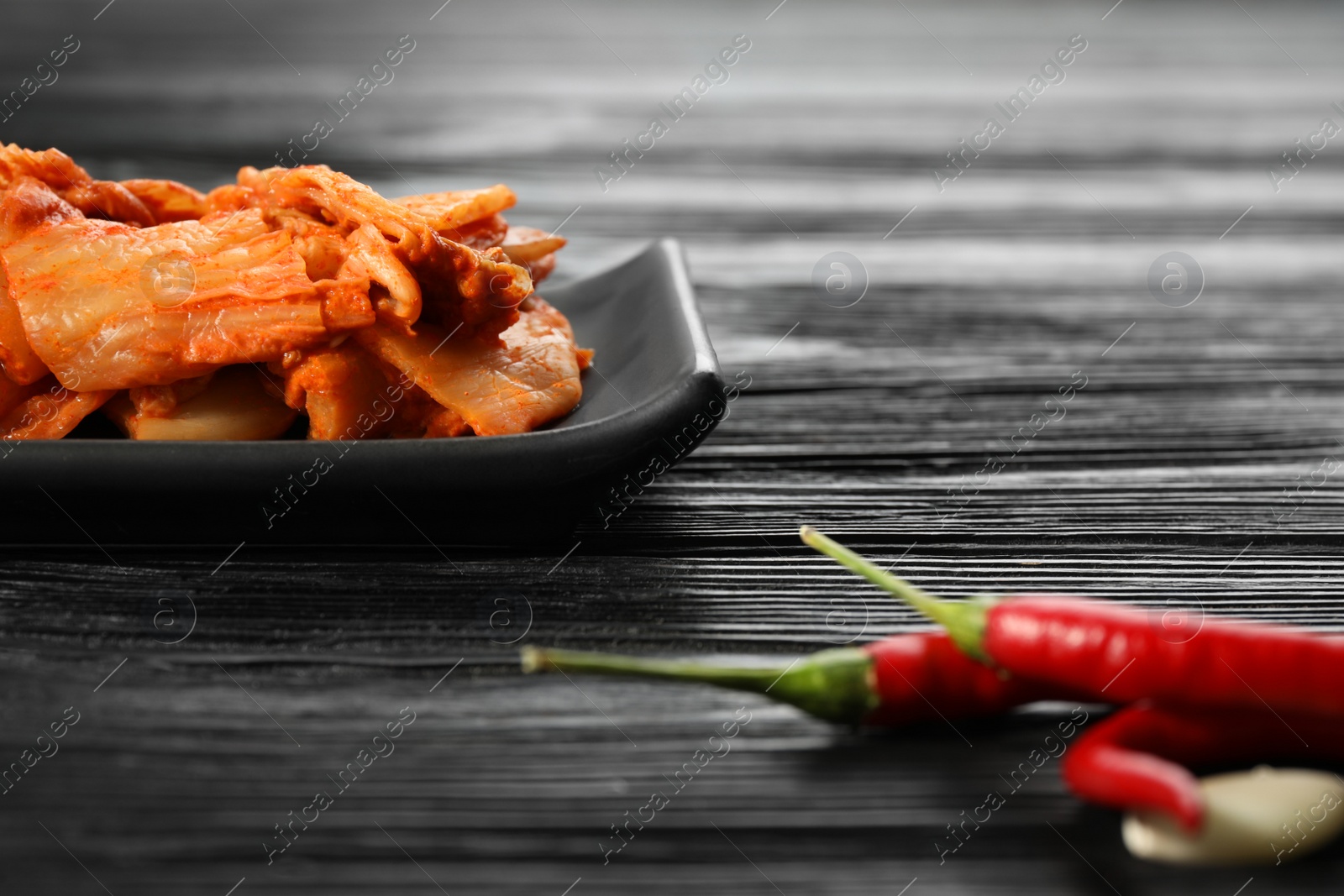 Photo of Delicious kimchi with Chinese cabbage, red chili peppers and garlic on black wooden table