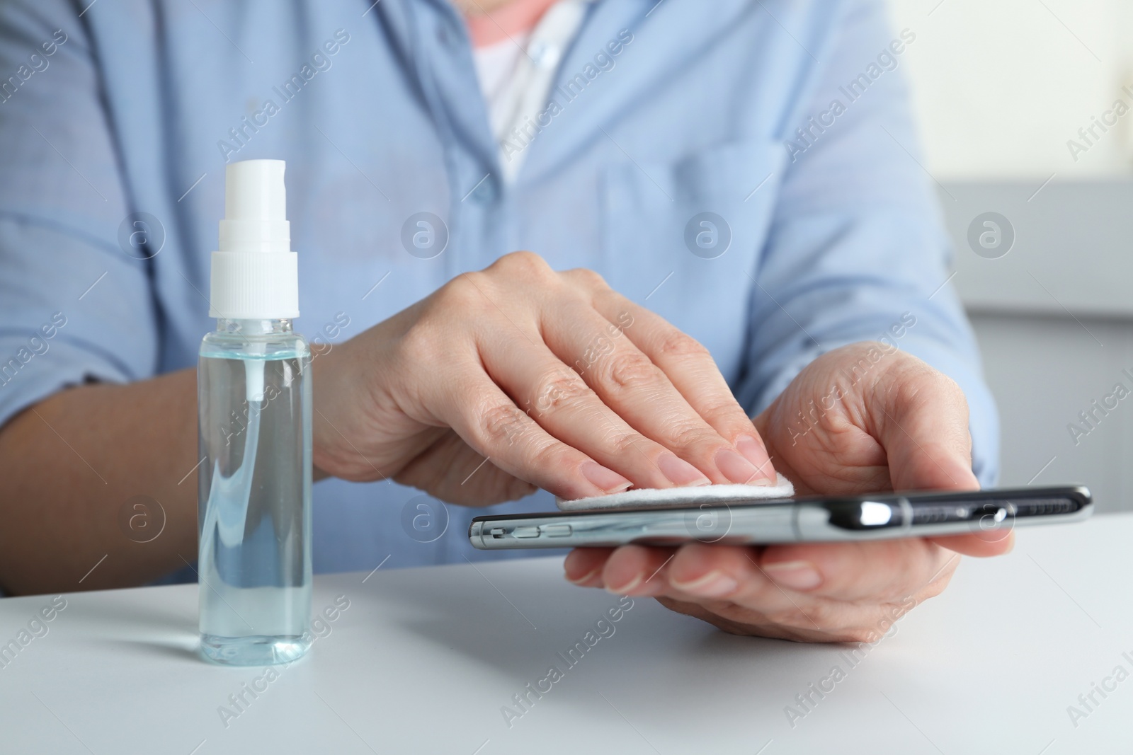 Photo of Woman cleaning smartphone with antiseptic at white table, closeup