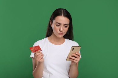 Photo of Confused woman with credit card and smartphone on green background. Debt problem