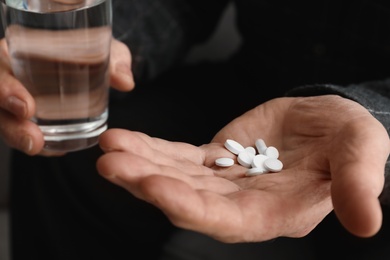 Senior man holding pills and glass of water, closeup