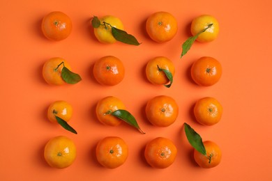 Photo of Delicious tangerines with green leaves on orange background, flat lay