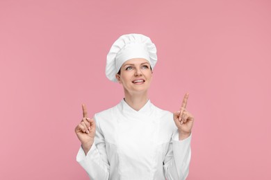Photo of Happy chef in uniform pointing at something on pink background