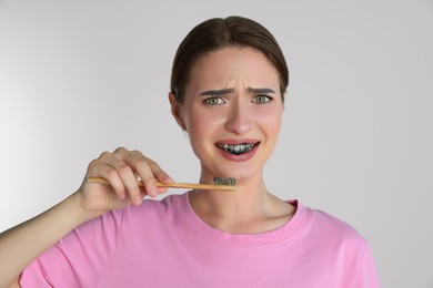 Photo of Young woman brushing teeth with charcoal toothpaste on light background