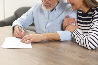 Senior couple signing Last Will and Testament at wooden table, closeup