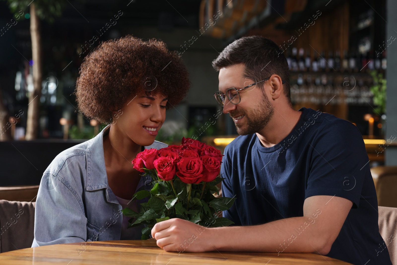 Photo of International relationships. Handsome man presenting roses to his beloved woman in cafe