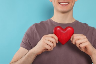 Happy volunteer holding red heart with hands on light blue background, closeup