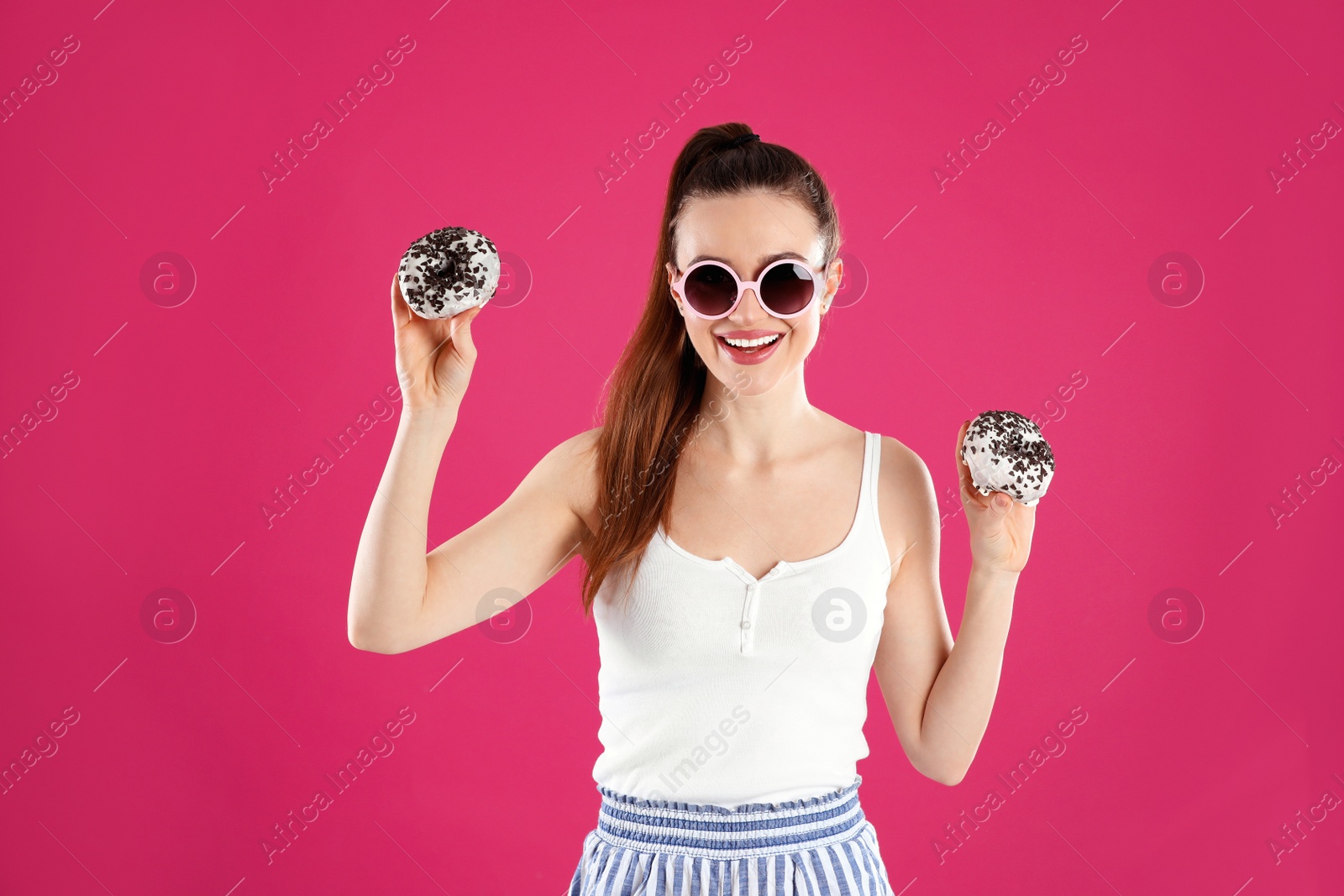 Photo of Beautiful young woman wearing sunglasses with donuts on pink background