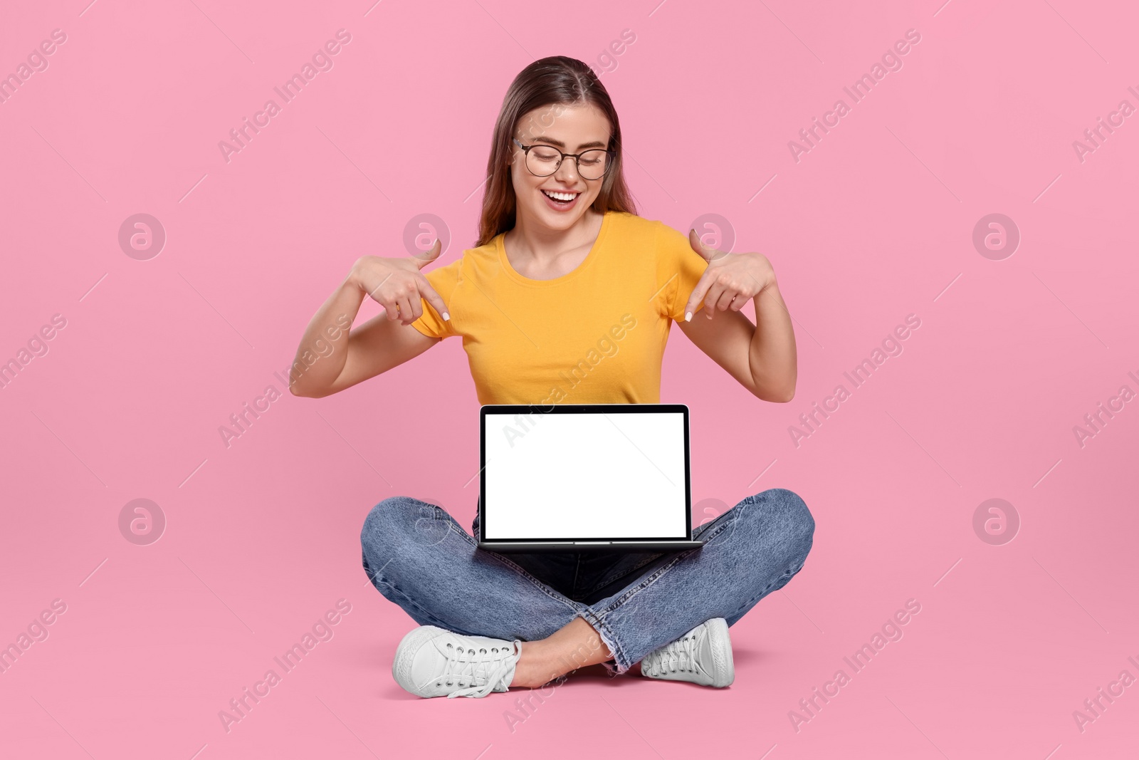 Photo of Happy woman in glasses pointing at laptop on pink background