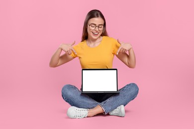 Happy woman in glasses pointing at laptop on pink background