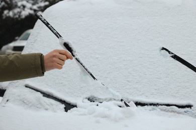 Photo of Woman cleaning car wiper blades covered with snow outdoors, closeup