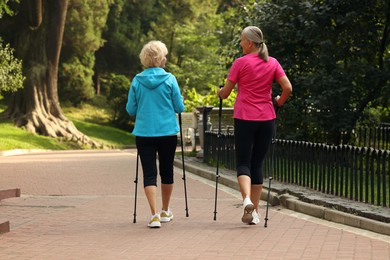 Photo of Two senior friends performing Nordic walking outdoors, back view