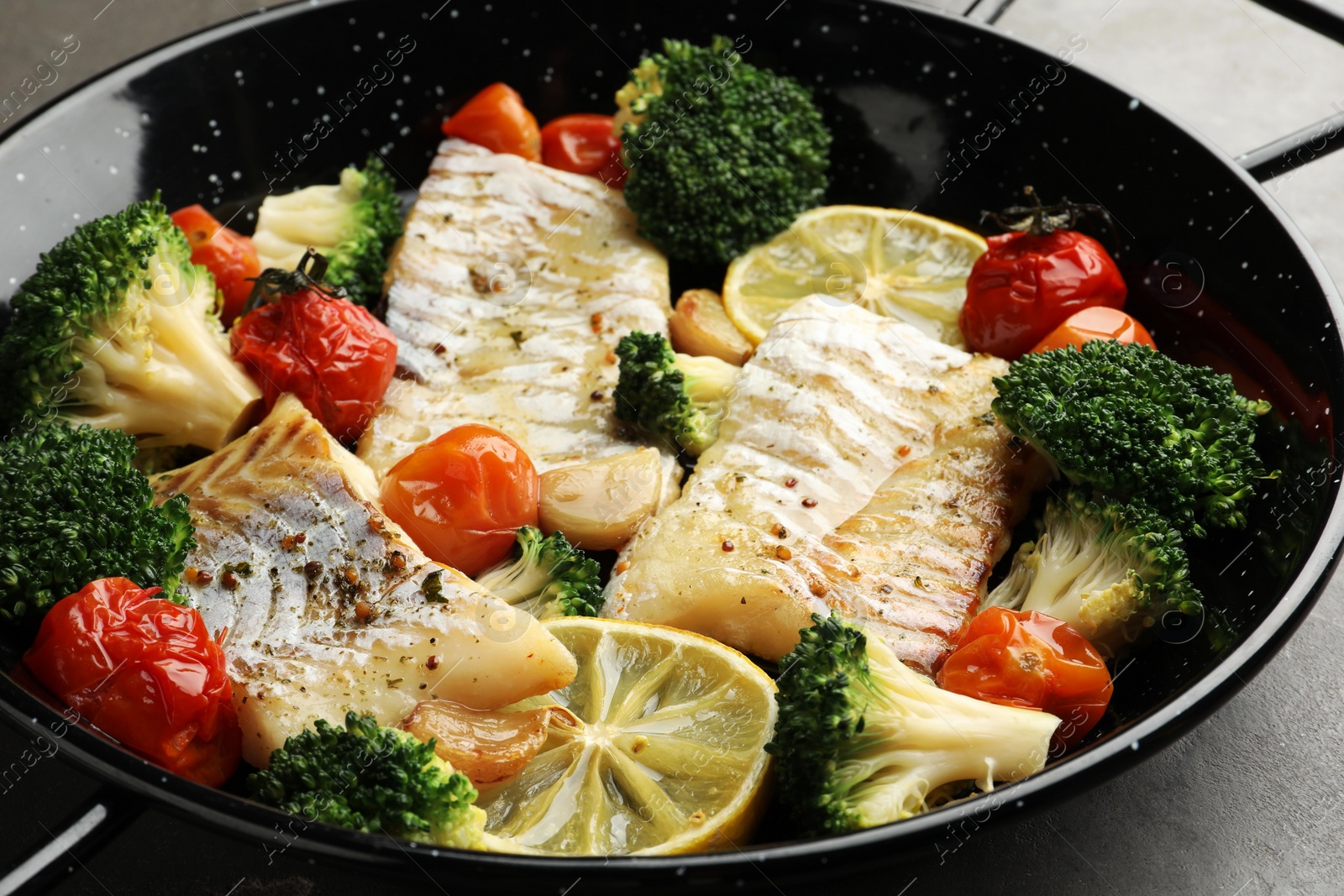 Photo of Tasty cod cooked with vegetables in frying pan on grey table, closeup