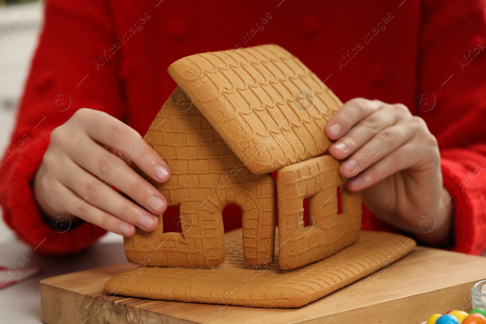 Photo of Woman in red sweater making gingerbread house, closeup