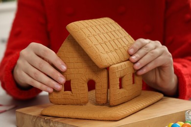 Photo of Woman in red sweater making gingerbread house, closeup