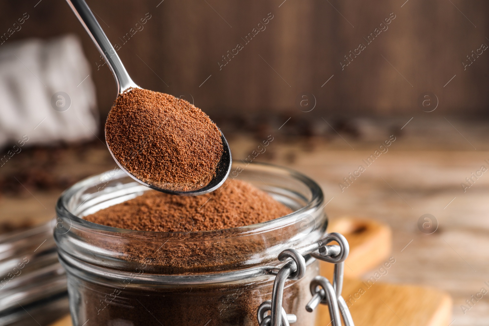 Photo of Instant coffee and spoon above glass jar on table, closeup