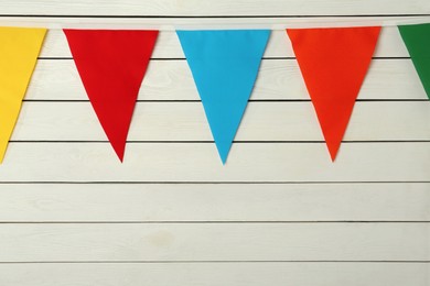 Bunting with colorful triangular flags on white wooden background, space for text