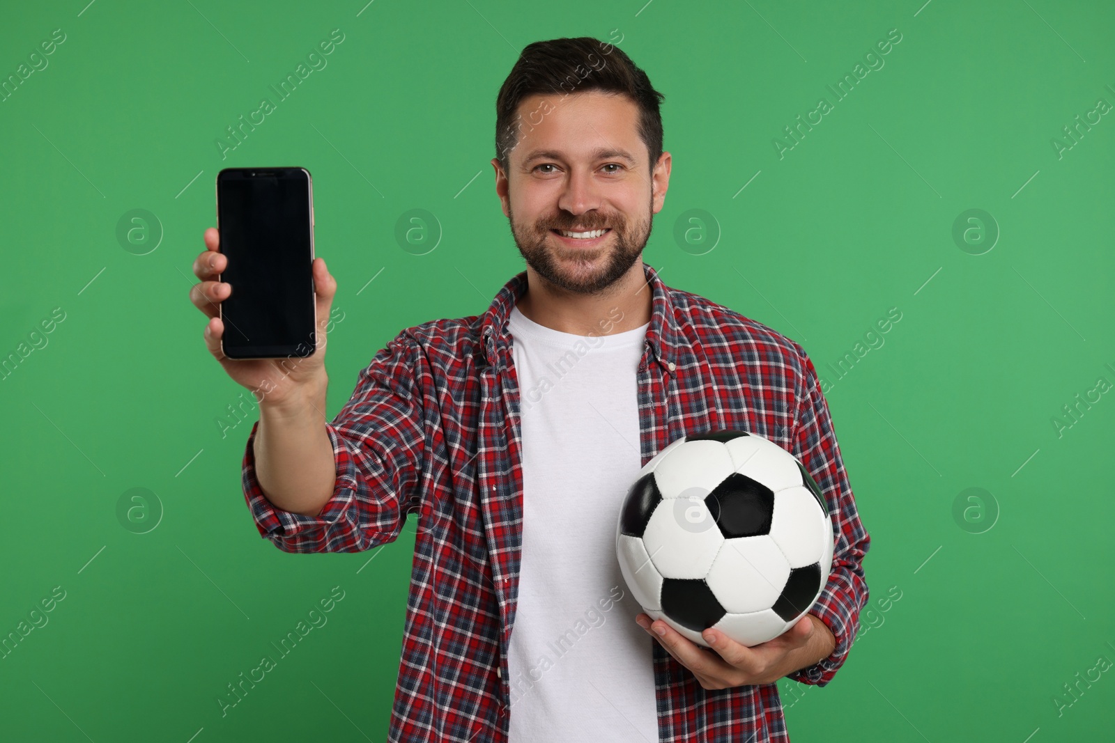 Photo of Happy sports fan with ball and smartphone on green background