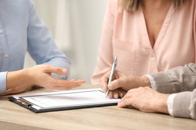 Photo of Notary showing senior man where to sign Last Will and Testament at wooden table, closeup