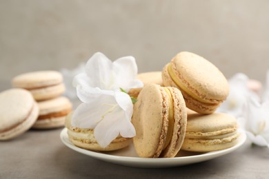 Photo of Delicious macarons and flowers on grey table