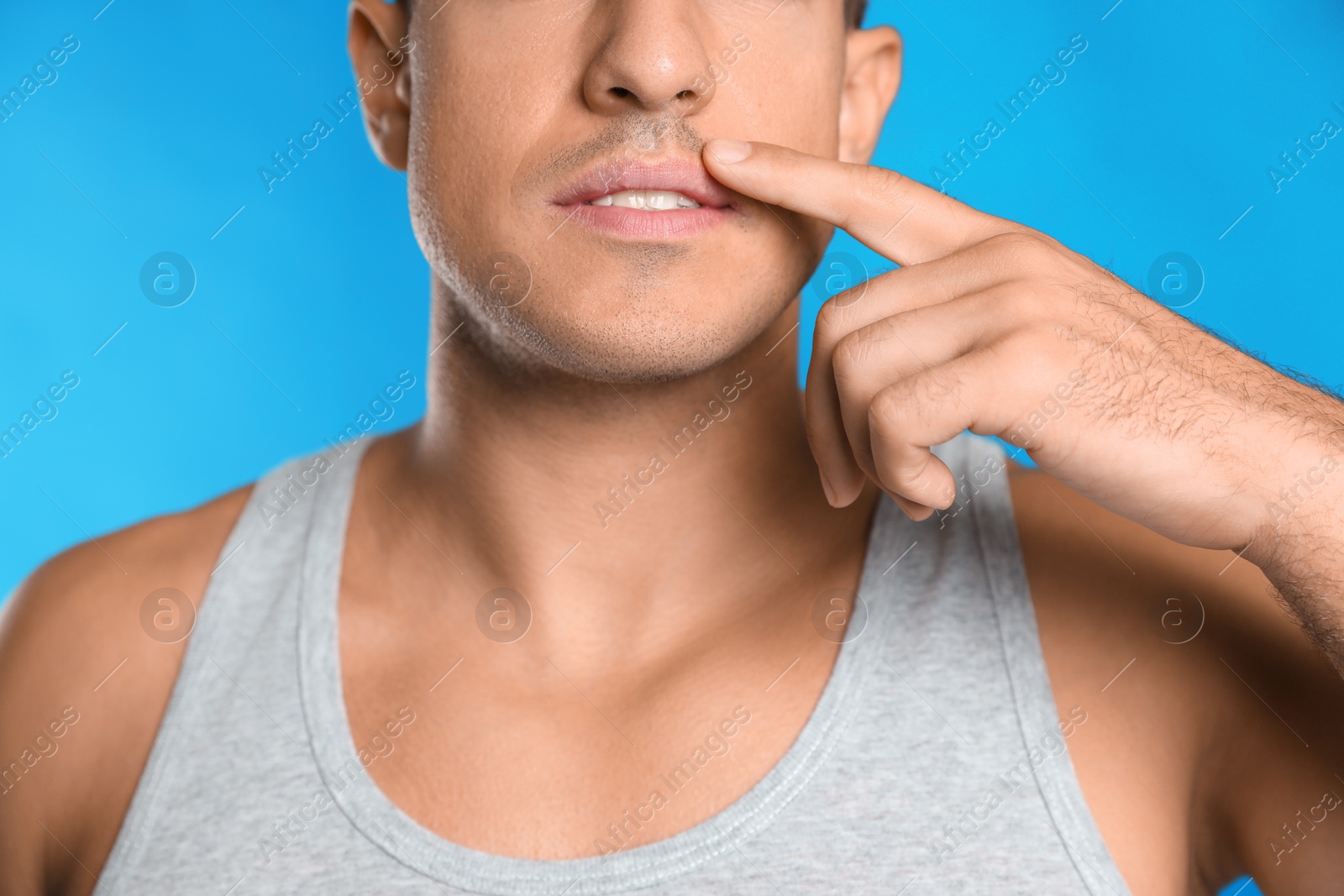 Photo of Man with herpes touching lips against light blue background, closeup