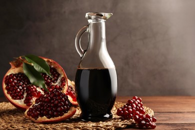 Photo of Glass jug of tasty pomegranate sauce and fresh ripe fruit on wooden table. Space for text