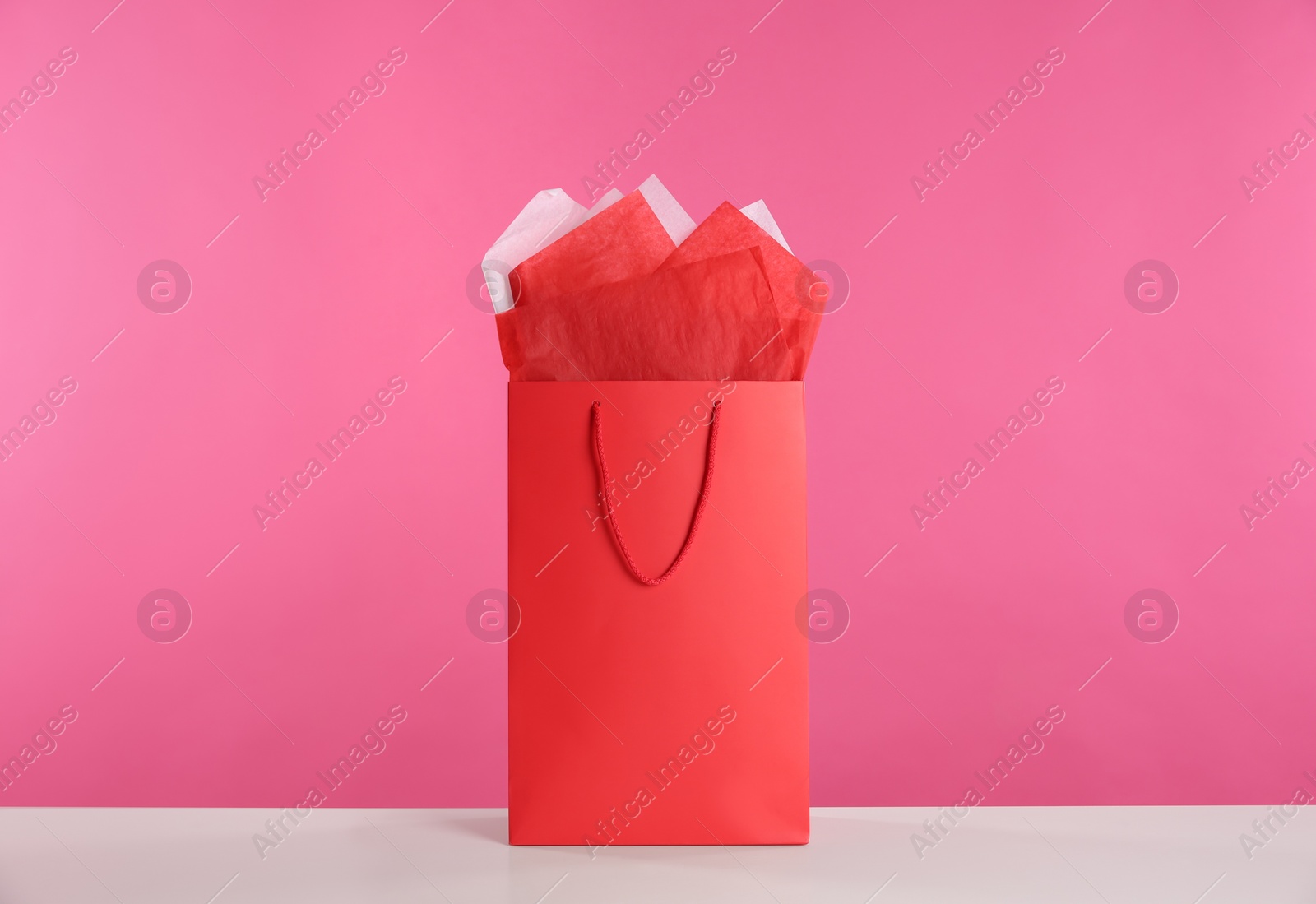 Photo of Gift bag with paper on white table against pink background