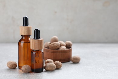 Photo of Bottles of nutmeg oil and nuts on light grey table. Space for text