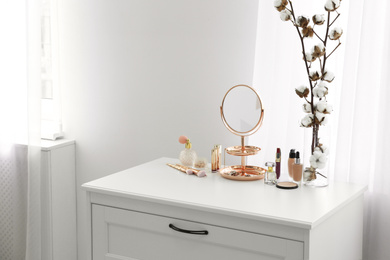 Photo of Small mirror and different makeup products on chest of drawers indoors. Space for text
