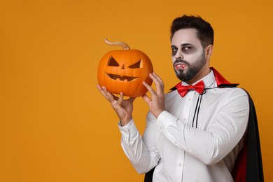 Photo of Man in scary vampire costume with fangs and carved pumpkin on orange background, space for text. Halloween celebration