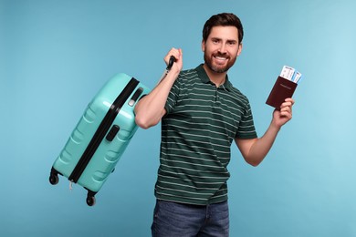 Photo of Smiling man with passport, suitcase and tickets on light blue background