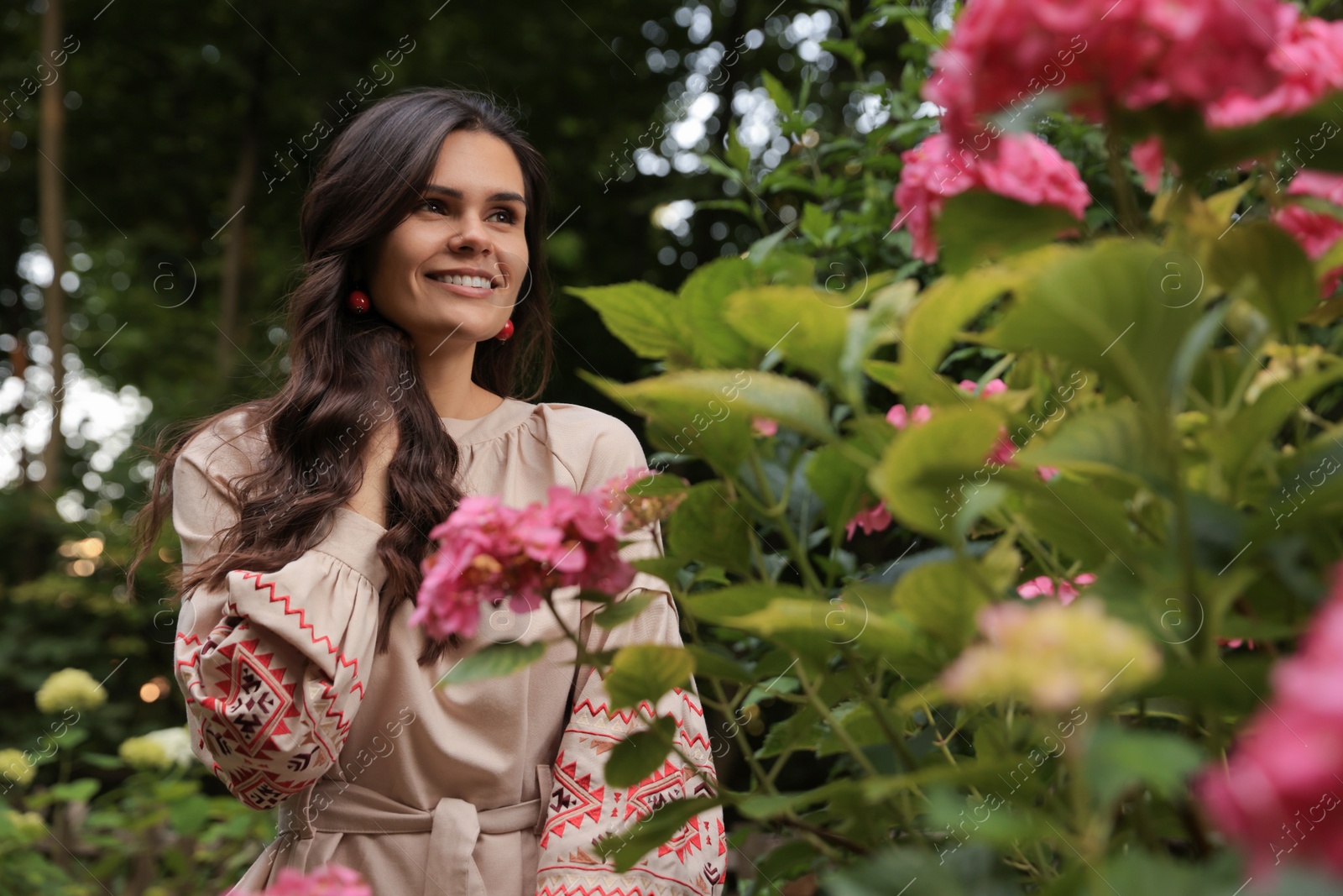 Photo of Beautiful woman wearing embroidered dress in blooming garden. Ukrainian national clothes