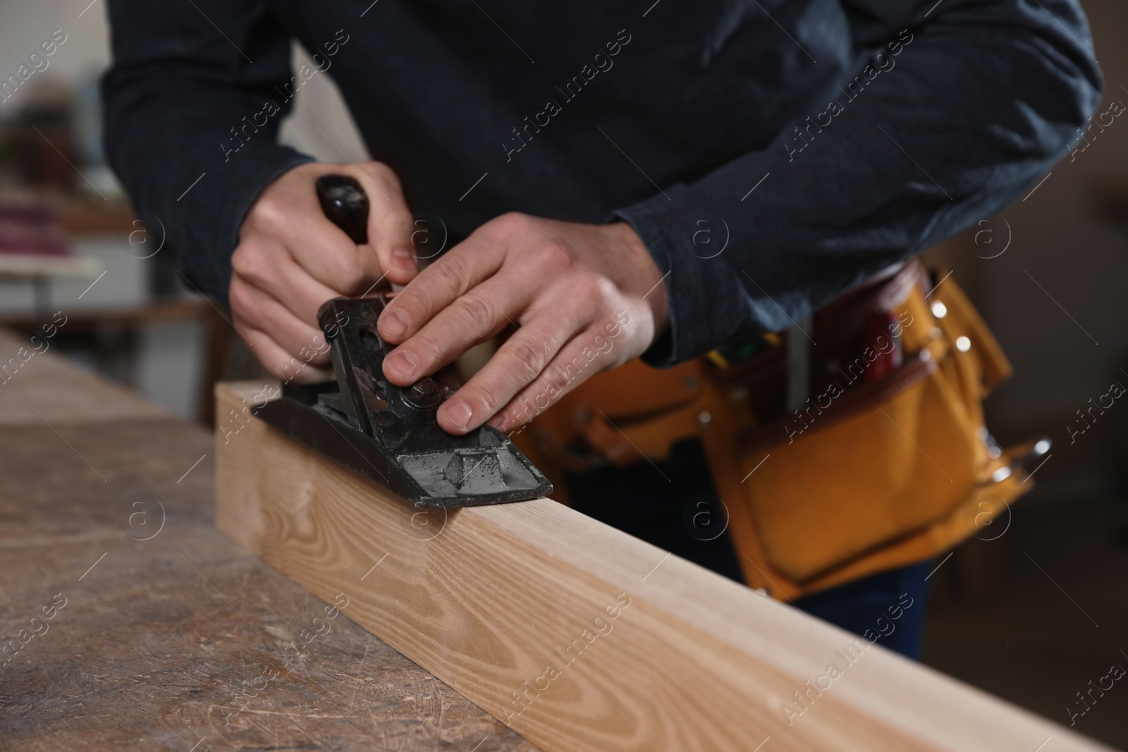 Photo of Professional carpenter grinding wooden plank with jack plane in workshop, closeup