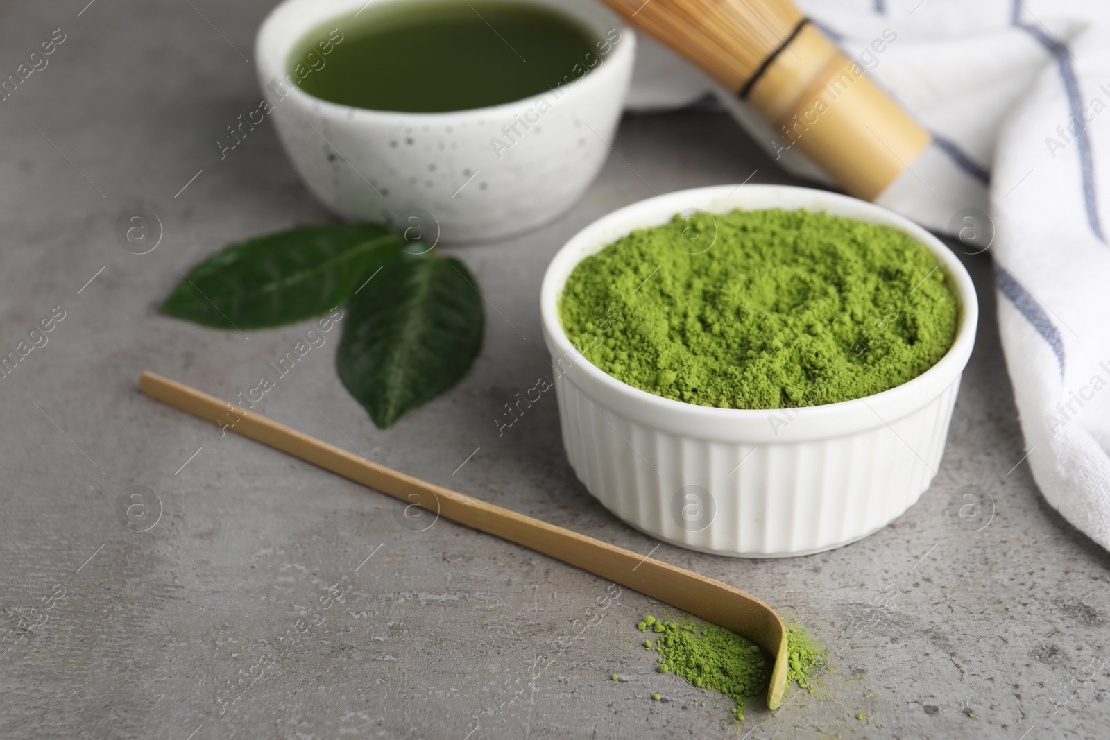 Photo of Green matcha powder and bamboo scoop on light grey table, closeup