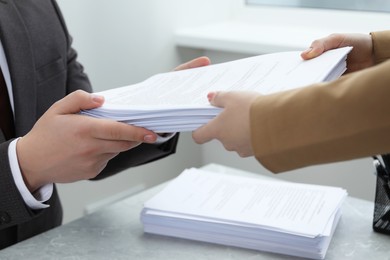 Photo of Woman giving many documents to man at table in office, closeup