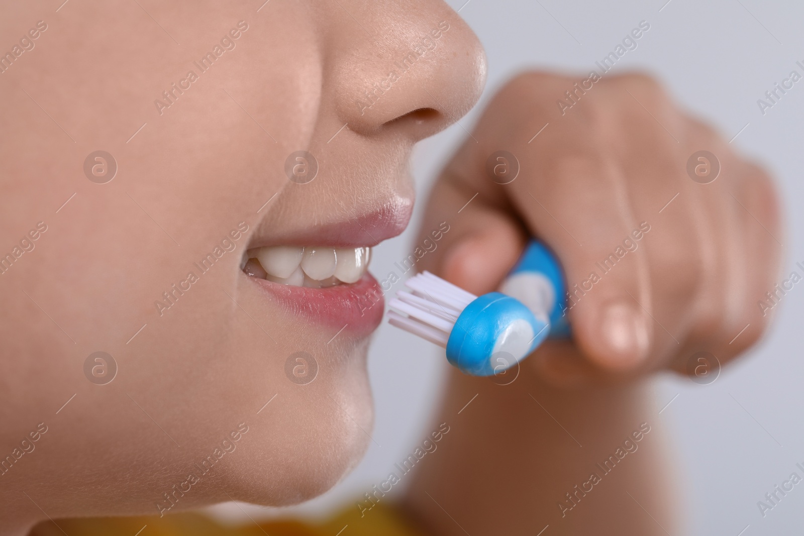 Photo of Girl brushing her teeth with toothbrush on light grey background, closeup