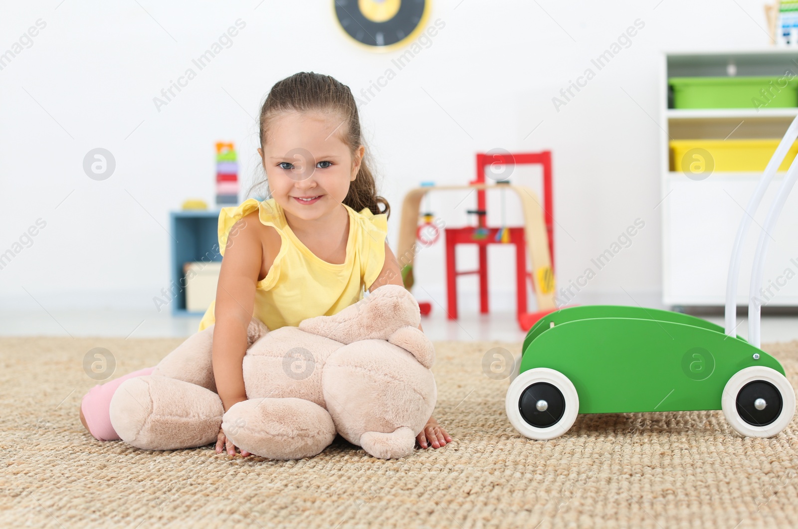 Photo of Cute little girl playing with teddy bear on floor at home. Soft toy