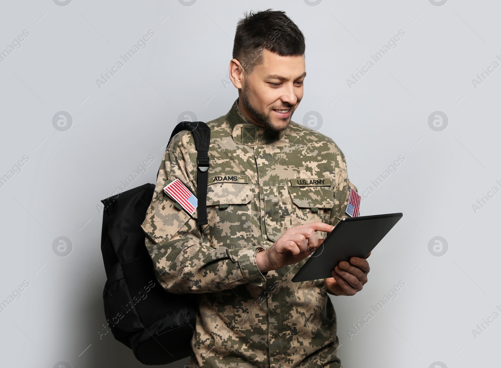 Photo of Cadet with backpack and tablet on light grey background. Military education