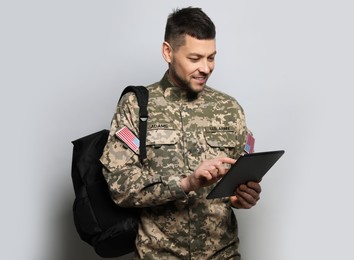 Photo of Cadet with backpack and tablet on light grey background. Military education