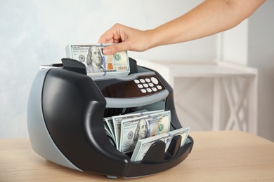 Photo of Woman putting money into counting machine at table indoors, closeup