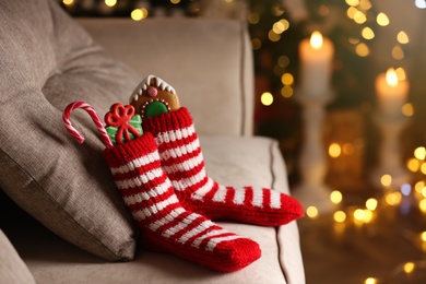 Photo of Socks filled with sweets on sofa in room, space for text. Saint Nicholas Day