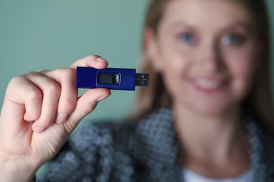 Woman holding usb flash drive against green background, focus on hand