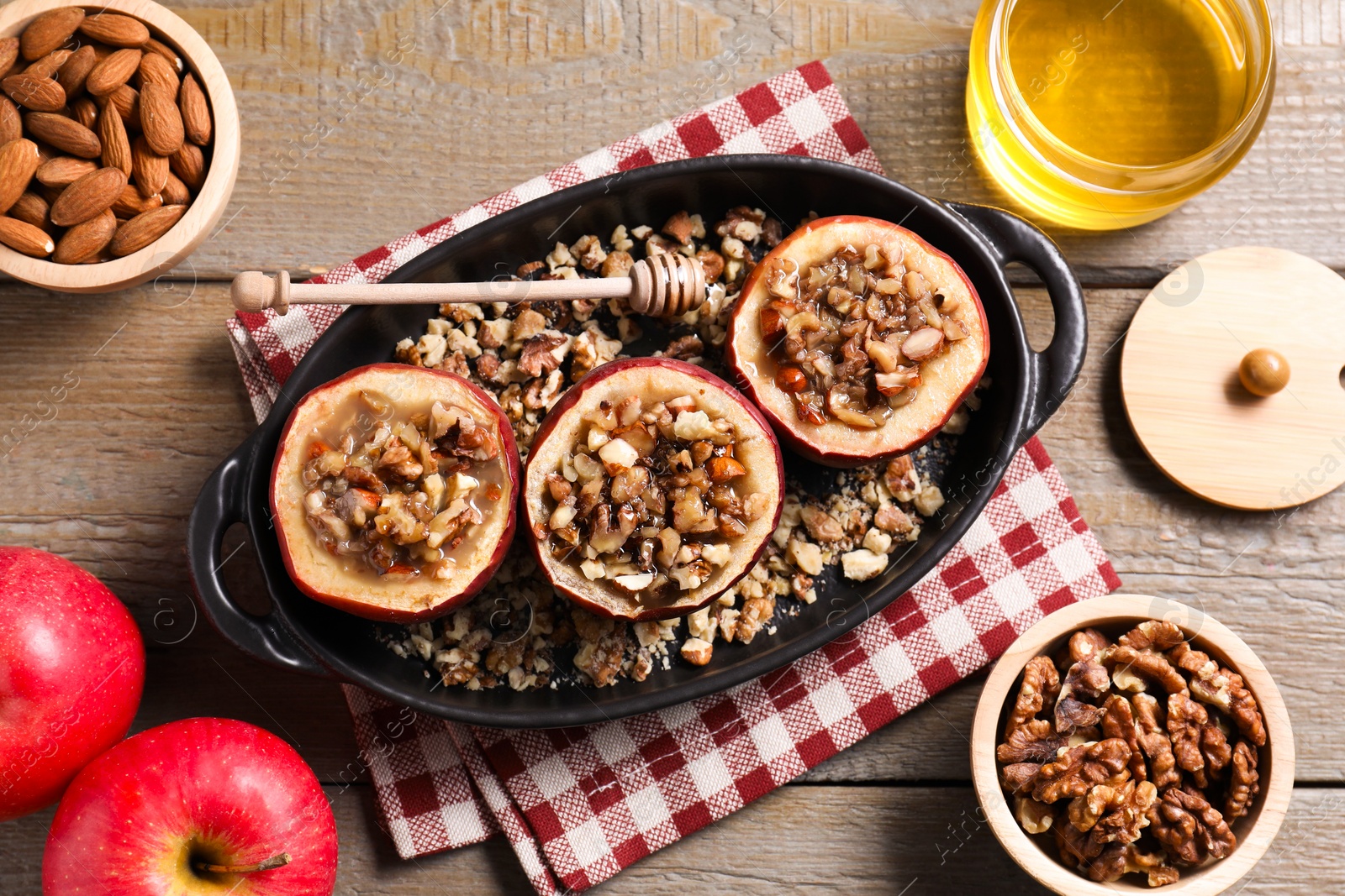 Photo of Tasty baked apples with nuts and honey in baking dish on wooden table, flat lay