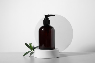 Bottle of cosmetic product and green leaves on light grey table against white background