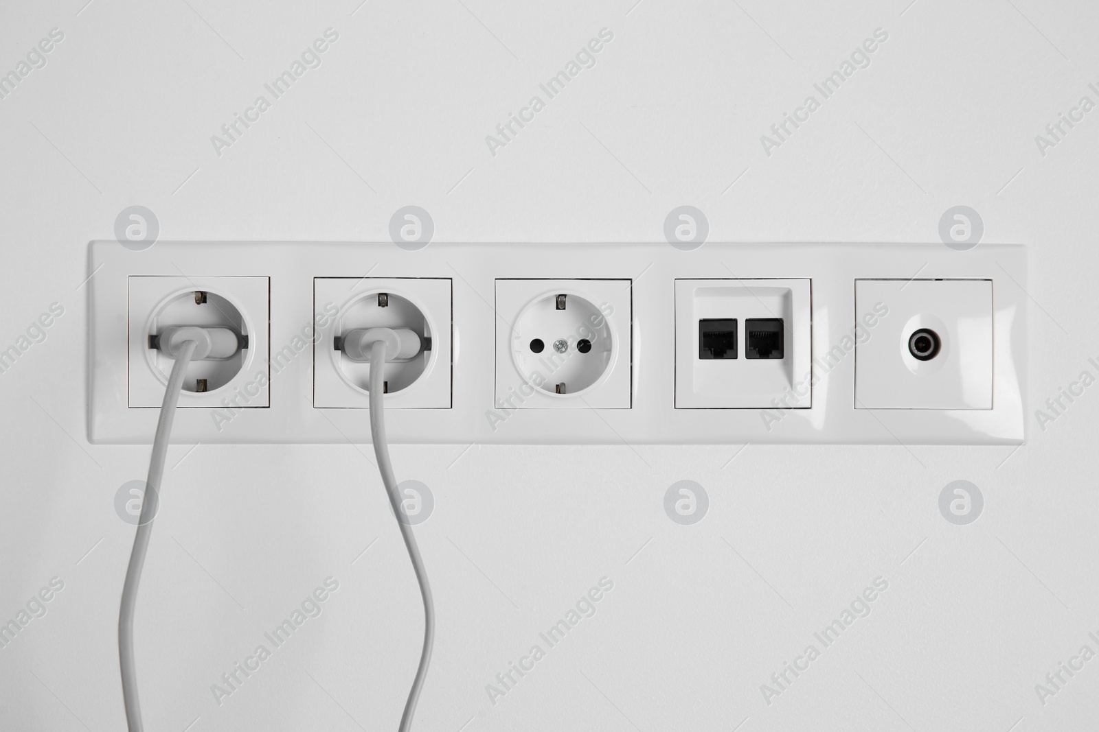 Photo of Many power sockets with plugs, ethernet and TV coax plates on white wall indoors