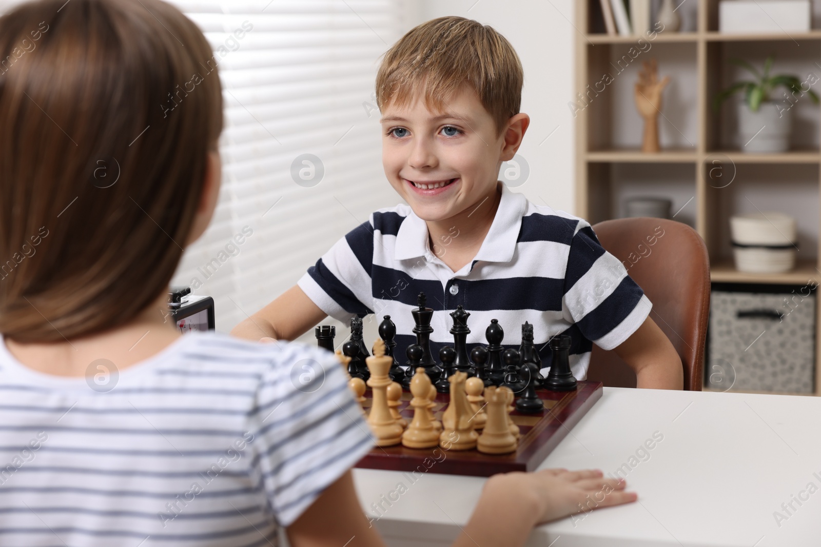 Photo of Cute children playing chess at table in room